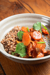 Buckwheat porridge with fish in a ceramic plate over rustic wooden background.