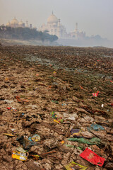 Bank of Yamuna river covered with garbage and Taj Mahal in a fog in the background, Agra, Uttar Pradesh, India