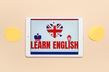 Tablet computer and blank speech bubbles on color background. Concept of learning English