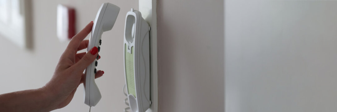Woman hand picks up intercom receiver in apartment