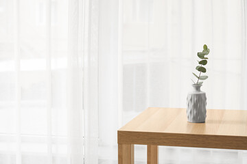 Table with vase near light curtains in room