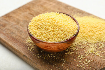 Bowl with raw couscous on wooden board, closeup