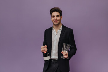Charming young brunette with light shirt, black suit holding bottle of champagne and two glasses,...