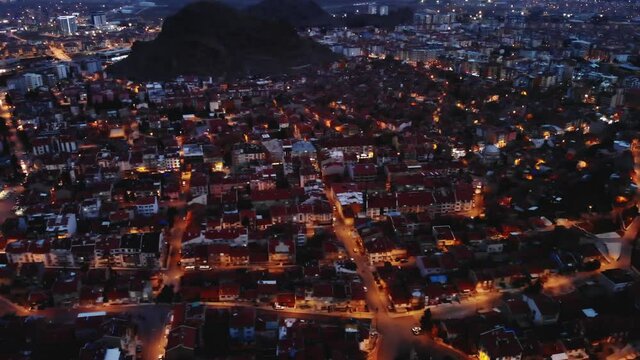 Scenic aerial view of Afyonkarahisar cityscape with lighted streets and similar reddish tiled roofs on residential buildings in winter twilight, Turkey