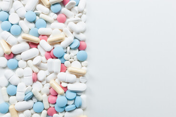 Pile of blue, white, pink and yellow colored pills and capsules on left side of white background with copy space on right