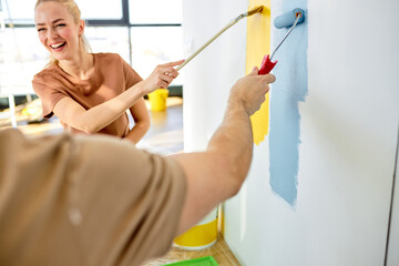 Happy couple painting walls in new house, using paint roller, brush, close-up photo of hands,caucasian man and woman renovate home interior together. copy space. rear view on cropped man