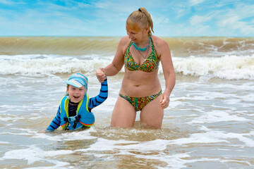 Fototapeta premium A woman takes a child in a life jacket out of the stormy sea