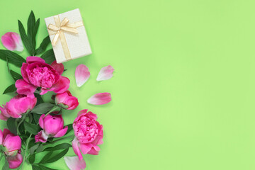 Bouquet of beautiful pink peonies with gift boxes in wrapping paper on green background. Festive greeting card.  Creative background with copy space for text.