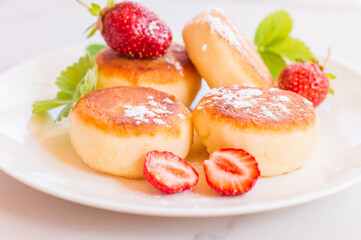 Syrniki, curd or cottage cheese pancakes withstrawberry, powdered suga on a white table
