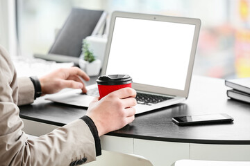 Young man with cup of coffee using laptop in office