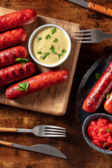Grilled German sausages with mustard sauce and ketchup, shot from above on a dark rustic wooden table. Wiener bratwurst, spicy gourmet food