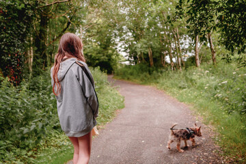 Teenager girl walking out small cute Yorkshire terrier in a park.