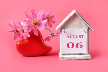  Calendar for: August 6 : the name of the month of August in English with the numbers 0 and: 6 on a toy house, a bouquet of pink flowers in a heart-shaped vase, pink background