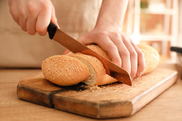Woman cutting fresh bread in kitchen, closeup