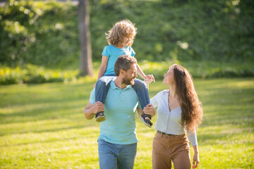 Happy family of mother and father carrying boy child on shoulders summer outdoors, foster