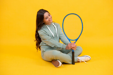 cheerful teen girl in sportswear hold tennis racquet on yellow background, sport