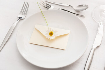 Stylish table setting, envelope and chamomile flower on light background