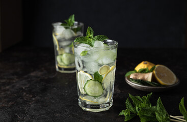 Detox Sassy Water. Cool and fresh drink with lemon, cucumber, mint, ginger and ice. Two glasses of lemonade on a black background. Copy space