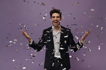 Gorgeous young brunette-haired man in white shirt and black suit smiling and posing with confetti...