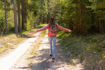 Young traveler girl arms outstretched enjoying the fresh air in the green summer spring forest.Sunny day.Back view