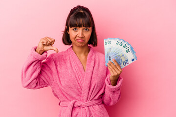 Young mixed race woman wearing a bathrobe holding bills isolated on pink background showing a dislike gesture, thumbs down. Disagreement concept.