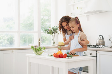 Mother and teen daughter preparing vegetable salad at kitchen