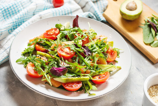 Salmon salad with green leaves, avocado and cherry tomato on concrete background