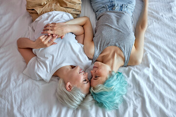 Obraz na płótnie Canvas Lesbian couple in the morning, happy wake-up, hugging and kissing, top view portrait on pretty ladies in domestic clothes spending weekends at home, relaxed and happy. copy space. people lifestyle