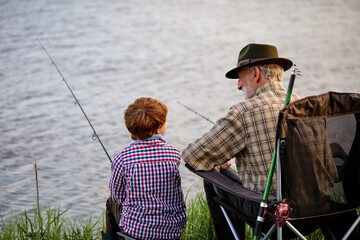 Caucasian senior fisherman teaching cute grandkids fishing on lake in nature, casually dressed....