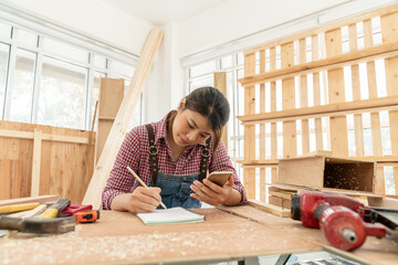 Portrait of females carpenter using mobile phone while checking list on the notebook