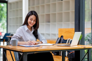 
Portrait of Business lady sitting at office table with various charts and reports and checking text messages in her laptop computer, charts and graphs banner,successful business planning concept.