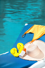 Swimsuit, hat, flip-flops and sunscreen cream on sun lounger near swimming pool