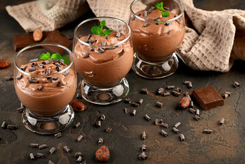 Vegan chocolate mousse with mint, bar of chocolate and cocoa beans on a dark background.