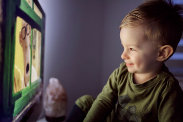 Fototapeta premium Entertaining the child before sleeping. The little boy is right in front of the TV and stares at the cartoon. The toddler laughs when his favorite cartoon character appears on the screen
