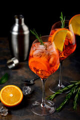 Wineglass of ice cold Aperol spritz cocktail served in a wine glass, decorated with slices of orange and rosemary branch. Black background