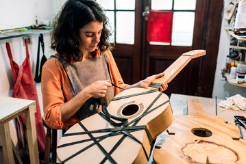 woman luthier making guitars in her musical instrument workshop