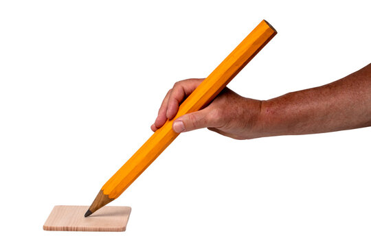 A male hand holds a very large yellow pencil isolated on a white background. The tip of the pencil rests on a light colored wooden board. Macro.