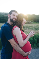 A married couple who are expecting a baby are photographed at sunset in a flower field. A pregnant woman and her loving man. The father kisses the belly in which his child is. Last terms of pregnancy