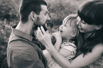 Fototapeta premium Happy family of three having fun and fooling around in the field. Dad, mom and daughter are playing and having fun in a flower meadow. Happy family concept with one child. Sincere smiles and laughter