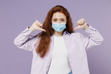 Young redhead curly woman 20s wears white T-shirt violet jacket sterile face mask ppe to safe from covid-19 flu on lockdown point on it isolated on pastel purple color wall background studio portrait.