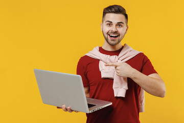 Smiling happy young man wear red t-shirt casual clothesuse point index finger on work on laptop pc computer isolated on plain yellow color wall background studio portrait. People lifestyle concept