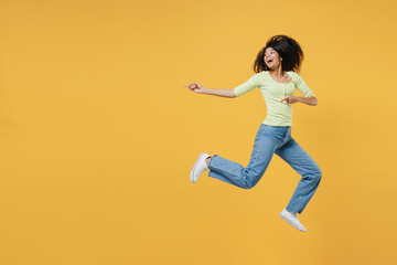 Fototapeta na wymiar Full size body length smiling overjoyed african american young woman 20s wears green shirt jump pointing back on workspace area copy space mock up closed isolated on yellow background studio portrait