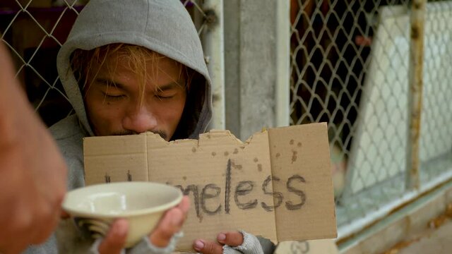 Homeless man with dirty clothes holding a cup and getting some money from kind peoples. 4K