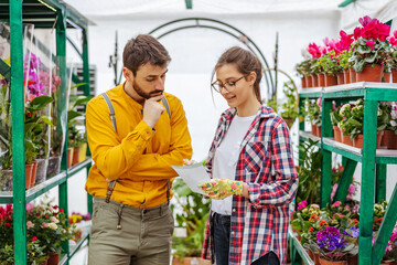Small business owner taking order from a customer. Man standing next to woman and telling her what he want. Greenhouse interior.