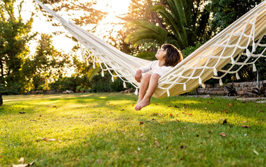 Cute little barefoot toddler boy relaxing in hammock in backyard garden looking at sky. Child...