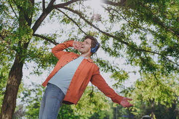 Bottom side view young man in orange jacket headphones leaning back walk listen music sing song...