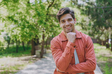 Young fun man 20s in orange jacket blue t-shirt walking look camera prop up chin rest relax in...