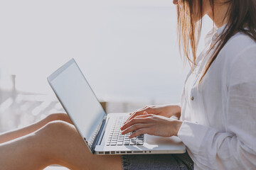 Cropped up photo shot young traveler tourist woman 20s in bandana shirt summer clothes rest sit on bench hold use work on laptop pc computer outdoors at sea beach Vacation lifestyle journey concept.