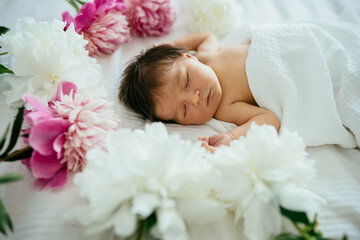 Obraz na płótnie Canvas Cute brunette hair caucasian newborn baby girl sleeping surround with flowers peonies on white bedroom at home. Close up.