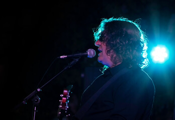 Man singing and playing bass on stage with backlit bright blue lights - live music event concept